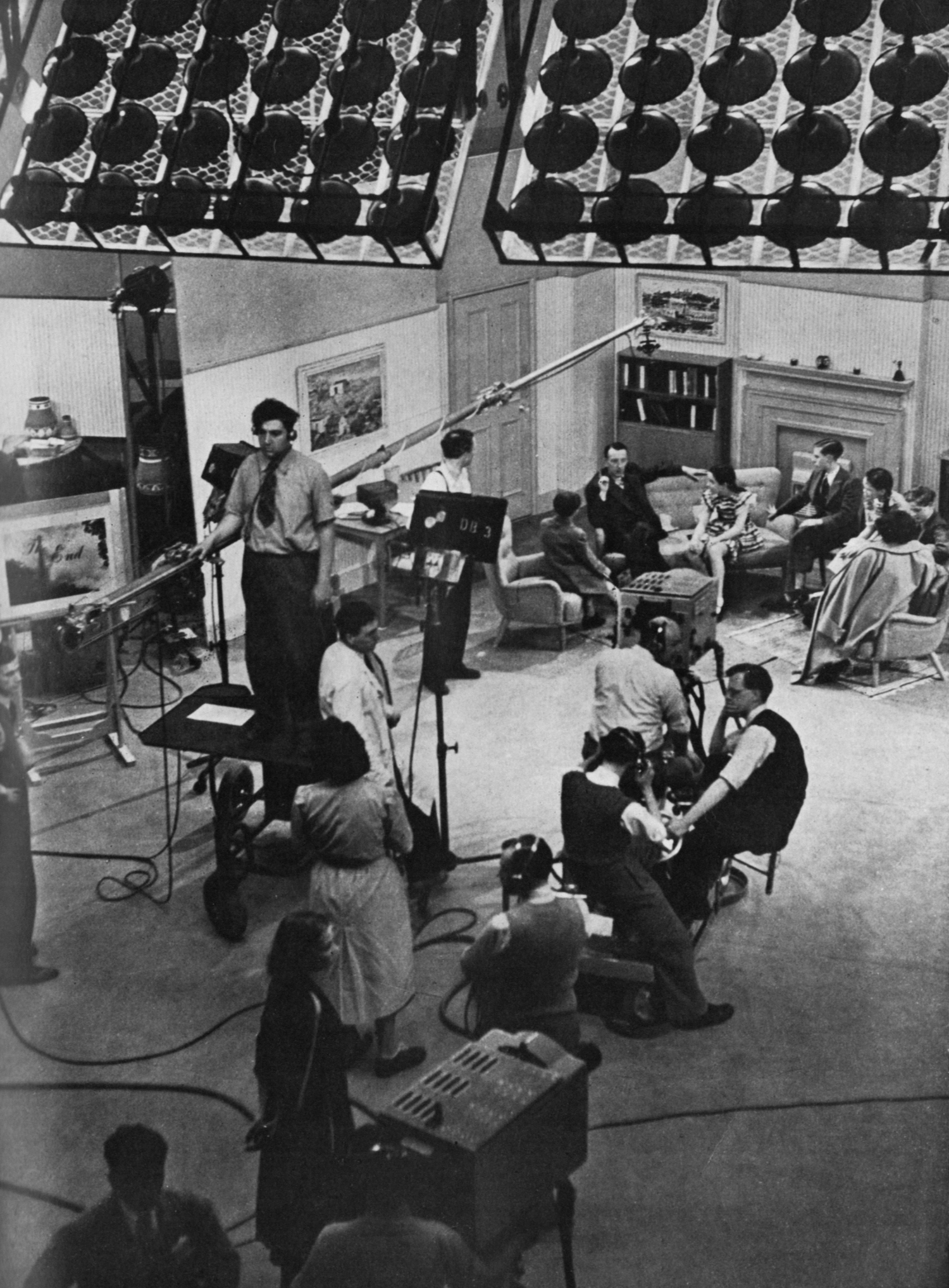 A view across a studio; people sit talking around a living room set