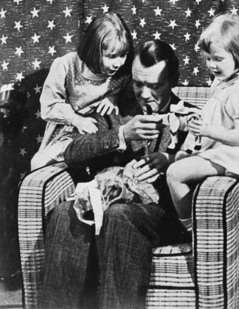 John Mills sits in an armchair with a child on each arm